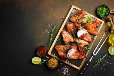 Tahtada soğan ve baharatla kızarmış tavuk kanadı. Karanlık bir arka planda.