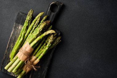 Kuşkonmaz hazırlama aşçılığı. Ahşap bir tahtanın üzerinde bir sürü kuşkonmaz. Karanlık bir taş arka planda. Üst görünüm.