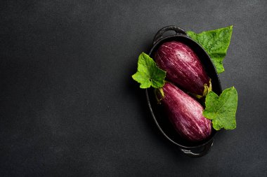 Siyah bir tabakta iki taze patlıcan. Siyah taştan bir arka planda. Metin için boş alan.