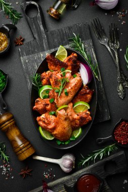 Limonlu, biberiyeli ve soğanlı kızarmış tavuk kanadı. Siyah bir tabakta. Karanlık bir arka planda.