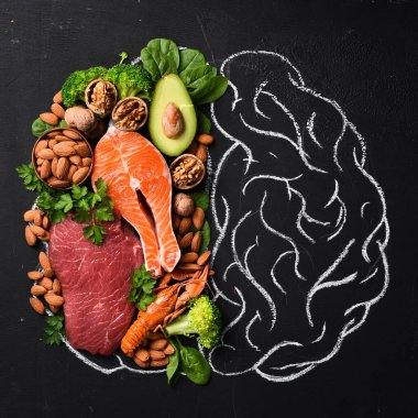 Beyin için sağlıklı besin kavramı: balık, et, fındık, sebze ve sebze. Tahtaya tebeşirle çizilmiş bir beyin. Üst Manzara. Siyah bir arkaplanda.