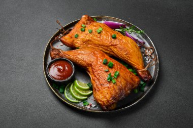 Siyah tabakta limon, biberiye ve baharatla tütsülenmiş tavuk bacağı. Karanlık bir arka planda.