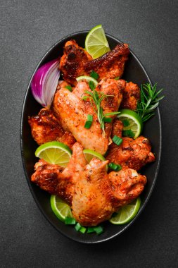 Limonlu, biberiyeli ve soğanlı kızarmış tavuk kanadı. Siyah bir tabakta. Karanlık bir arka planda.