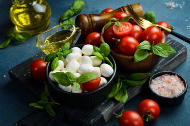 İtalyan Mozzarella peynirli topları, fesleğen ve domates kirazı Caprese salatası pişirmeye hazır. Karanlık bir taş arka planda.