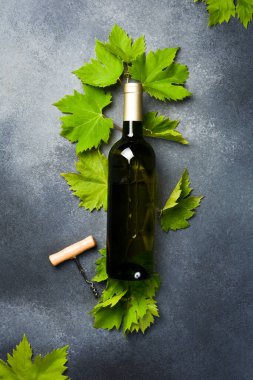 Arka planda üzüm yaprakları, tirbuşon ve şarap mantarları olan bir şişe şarap. Gri beton bir yüzeyde.