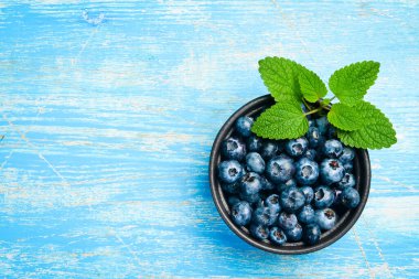 Yaban mersinli siyah taş kase. Mavi ahşap bir arka planda. Böğürtlenler yakın çekim.