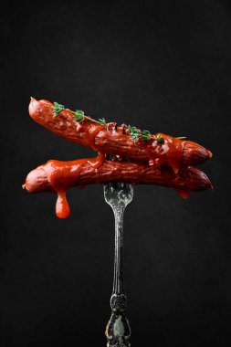 Ketçaplı sıcak Bavyera sosisi ve çatallı kekik. Siyah bir arkaplanda.