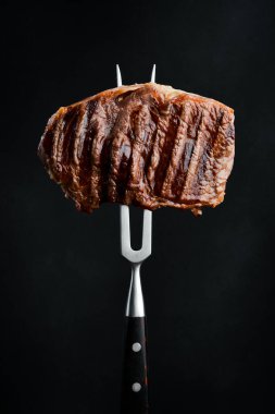 Çatallı, sulu biftekli biftek. Izgara biftek. Siyah bir arkaplanda.