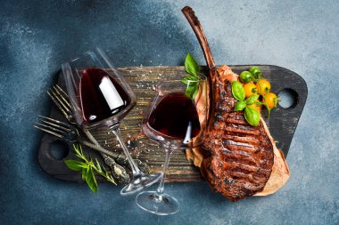 Bardakta şarap ve kemikte ızgara biftek. Gri beton arka planda. Metin için boş alan. Üst görünüm.