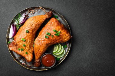 Siyah tabakta limon, biberiye ve baharatla tütsülenmiş tavuk bacağı. Karanlık bir arka planda.