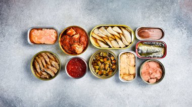 Konserve balık ve deniz ürünleri: ton balığı, somon yumurtası, lahanası, morina ciğeri ve uskumru. Bir ışık taşı arka planında.