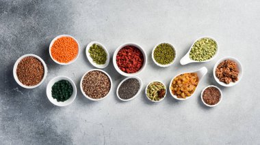 Süper yiyecekler, tahıllar, fındıklar ve kuru meyveler beyaz seramik kaselerde. Beyaz bir taş masanın üzerinde..