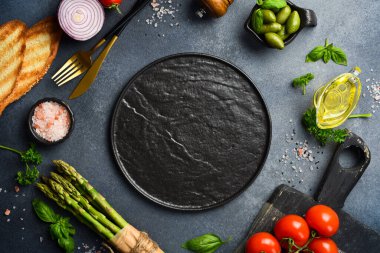 Tasarım için maket. Pişirme arka planı: siyah taş tabak, taze sebzeler ve gri beton arka planda baharatlar. Metin için boş alan.