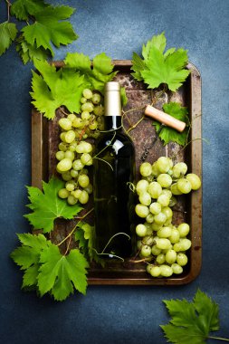 Beyaz şarap şişeleri, üzümler, bardaklar, tirbuşon ve siyah desenli masa mantarları. Üst görünüm.