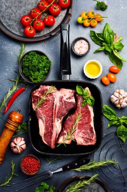 Tavada çiğ T-Kemik Bifteği. Gri bir masada biftek, baharat, baharat, tereyağı ve tuz pişirmek..