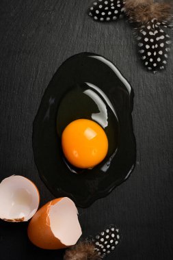 Sade bir yüzeyde kırılmış çiğ tavuk yumurtasının yakın çekimi. Siyah taştan bir arka planda. Üst görünüm.