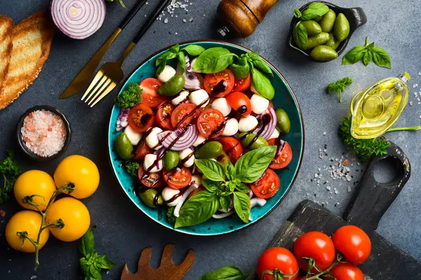 Taze yaz salatası: domates, mozzarella peyniri, fesleğen ve zeytin. Caprese. Gri beton arka planda.