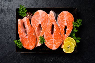 Somon balığı. Baharatlı çiğ somon bifteği, limon ve sarımsak metal tepside pişirmeye hazır. Karanlık bir taş arka planda. Üst görünüm.