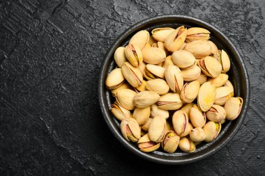 Çam fıstığı. Kavrulmuş fıstıklı siyah taş kase. Makro fotoğraf, yakın plan. Siyah taştan bir arka planda.