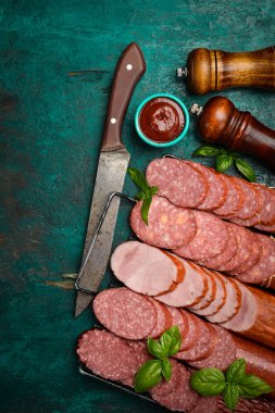 Farklı türde salam, kağıt ve tütsülenmiş sosisler. Koyu taş bir masada dilimlenmiş. Somut bir geçmiş. Üst görünüm.