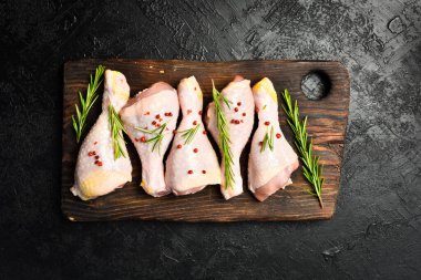 Çiğ tavuk budu, baharat ve otlarla ahşap bir kesme tahtasının üzerinde. Kalıplaşmış bir taş arka planda.