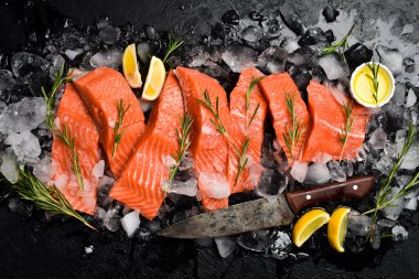 Buzlu taze çiğ somon bifteği, biberiye ve limon. Siyah taşlı arka planda balık filetosu. Üst görünüm.