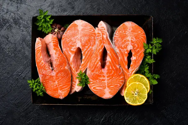 Somon balığı. Baharatlı çiğ somon bifteği, limon ve sarımsak metal tepside pişirmeye hazır. Karanlık bir taş arka planda. Üst görünüm.