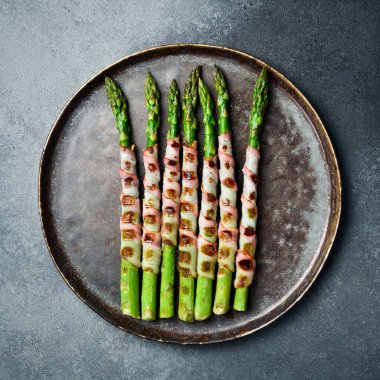 Taş tabakta domuz pastırmalı kızarmış kuşkonmaz. Üst görünüm.