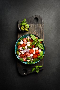Bir kasede Caprese salatası: domates, mozzarella peyniri, fesleğen ve zeytin. Siyah taştan bir tuvalde. Minimalizm tarzı. Üst görünüm.