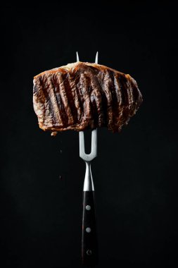 Çatallı, sulu biftekli biftek. Izgara biftek. Siyah bir arkaplanda.