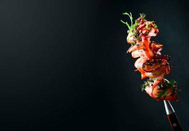 Biberiyeli pastırma dilimleri ve metal çatallı baharatlar. Siyah bir arkaplanda, yakın plan.