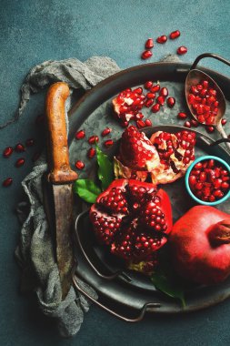 Yakından bakınca bir kâse dolusu nar, açık nar ve nar çekirdeği görülebiliyor. Beton bir arka planda. Üst görünüm.