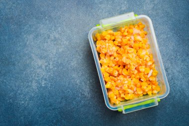 Plastik kutuda dondurulmuş mısır. Kış için dondurulmuş sebzeler. Gri taştan bir arka planda. Yakın plan..