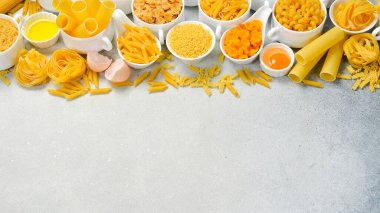 Makarna arka planı. Açık beton zemin üzerinde farklı türde makarna içeren kompozisyon, üst görünüm.