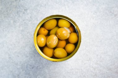 Metal kavanozda yeşil zeytin turşusu. Gri beton arka planda.