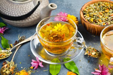 Sağlıklı bir fincan bitki çayı, kuru çay ve çiçekli kompozisyon. Gri beton arka planda. Dikey fotoğraf.