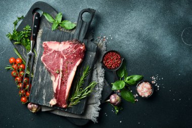 Kurumuş Raw T-bone ya da biftekli ve otlu biftek. Siyah taştan bir arka planda. Barbekü.