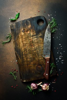 Kesme tahtası, biberiye ve baharatlar eski ahşap bir masada. Karanlık bir arka planda. Tarif için boş alan.