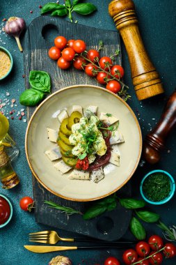 Patates ve turşulu tuzlu ringa balığı. Tabakta. Restoran servisi. Kapatın. Karanlık bir taş arka planda.