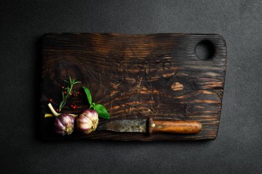 Kesme tahtası, biberiye ve baharatlar eski ahşap bir masada. Karanlık bir arka planda. Tarif için boş alan.