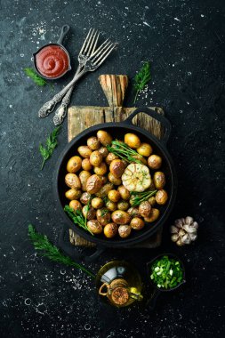 Fırında pişmiş patatesler tavada iştah açıcı. Sarımsaklı, otlu ve baharatlı Rustik fırında patates. Siyah taştan bir arka planda.