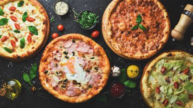 Pizza arka planı. Siyah taş arka planda lezzetli pizza ve malzeme seti. Üst görünüm.