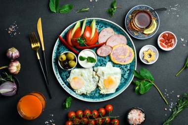 İngiliz kahvaltısı. Kızarmış yumurta, salam, pastırma ve sebze. Çay ve tatlı. Koyu bir arkaplanda.