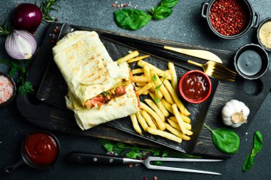Fast food: sosisli ve sebzeli burrito ve soslu patates kızartması. Karanlık bir arkaplanda, yakın plan.