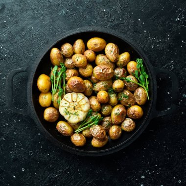 Fırında pişmiş patatesler tavada iştah açıcı. Sarımsaklı, otlu ve baharatlı Rustik fırında patates. Siyah taştan bir arka planda.