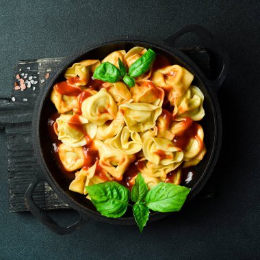 Domates soslu, etli ve fesleğenli geleneksel ravioli. En üstteki görünüm, koyu taştan bir arkaplan.