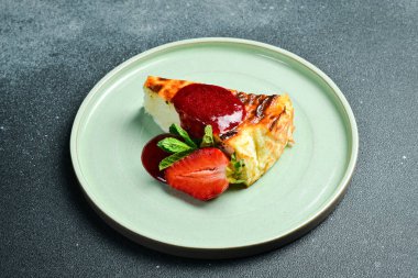 Peynirli kek. Çilek soslu bir dilim cheesecake. Karanlık bir taş arka planda.