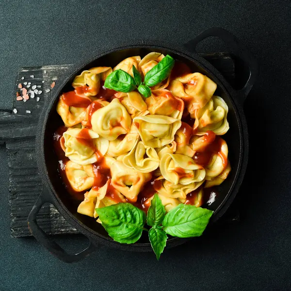 Domates soslu, etli ve fesleğenli geleneksel ravioli. En üstteki görünüm, koyu taştan bir arkaplan.