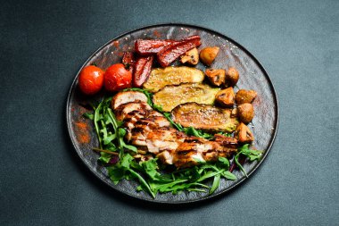 Izgara tavuklu fileto ve ızgara sebze tabağı. Barbekü menüsü. Karanlık bir arkaplanda, yakın plan.