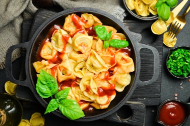 Domates soslu, etli ve fesleğenli geleneksel ravioli. En üstteki görünüm, koyu taştan bir arkaplan.